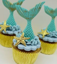 three cupcakes with blue frosting and gold decorations on them, each decorated as a mermaid's tail