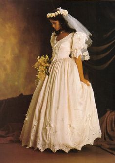 a woman in a white wedding dress with a veil on her head and flowers in her hair