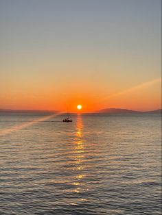 the sun is setting over the ocean with a small boat in the water below it