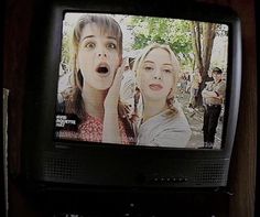 a tv with two people on it in front of a group of people standing around