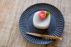 a small piece of food on a black plate with chopsticks next to it