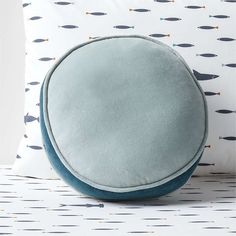 a round pillow sitting on top of a white table next to a blue and green pillow