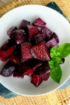 a white bowl filled with beets and basil on top of a wooden tablecloth