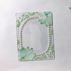 a white beaded necklace with green leaves and butterflies on it, sitting in front of a mirror