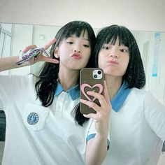 two young women taking a selfie in front of a mirror with their cell phones