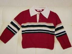 a red sweater with green, white and blue stripes on the collar is sitting on a couch