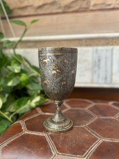 an old metal cup sitting on top of a leather ottoman next to a planter