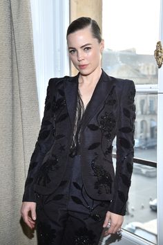 a woman standing in front of a window wearing a black suit with sequins