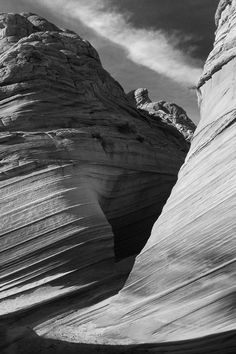 a black and white photo of the side of a rock formation with clouds in the sky