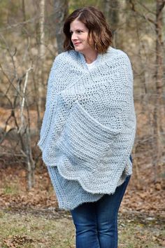 a woman is walking in the woods wearing a blue knitted ponchy sweater