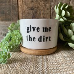 a coffee mug with the words give me the dirt on it next to some succulents