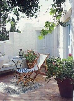 an outdoor patio with chairs, table and potted plants on the side of it