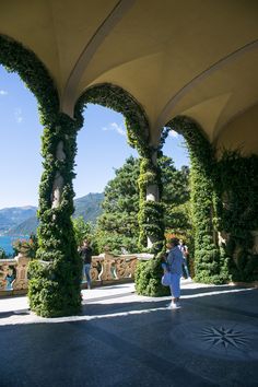 a person walking under an arch covered in greenery next to the ocean and mountains