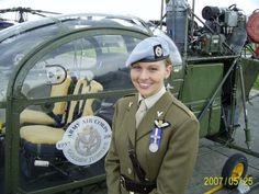 a woman in uniform standing next to a green helicopter with stuffed animals on the cockpit