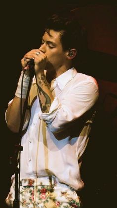 a man singing into a microphone while wearing a white shirt and floral pants on stage