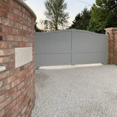 a brick wall and gate in front of a stone driveway with gravel on the ground