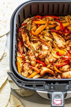 chicken fajita with peppers and onions in an air fryer basket next to tortillas