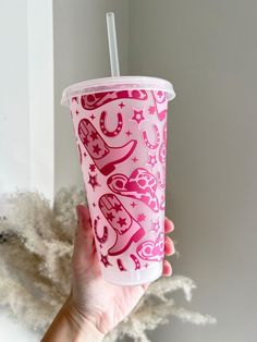 a hand holding up a pink cup with stars and hearts on the outside, in front of a white wall