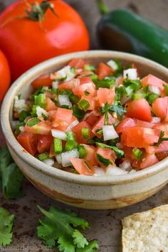 a small bowl filled with salsa next to some tortilla chips and two tomatoes