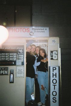 three young women standing in front of a photo booth at night with their arms around each other