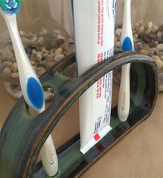 two toothbrushes sitting on top of a metal holder with rocks in the background