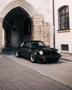 a black porsche parked in front of a white brick building with arched doorways and windows