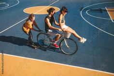 three people are riding on a bike in the middle of a basketball court while another person is standing next to them