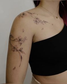 a woman wearing a black top with flowers on her arm and chest tattooing it