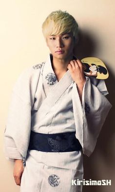 a young man in a kimono holding a paddle and looking at the camera while standing against a wall