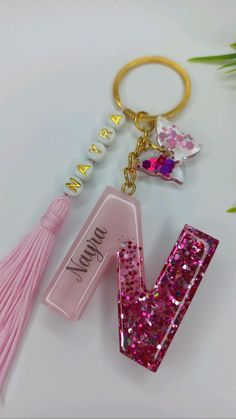 a pink letter shaped keychain with a tassel hanging from it's side