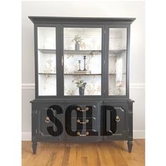 a black china cabinet with glass doors and gold handles on the bottom, in front of a wooden floor