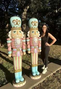 a woman standing next to two large wooden nutcrackers in front of a tree