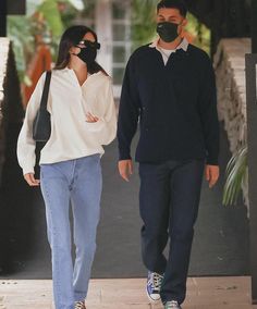 the man and woman are walking down the street wearing masks on their faces as they walk together