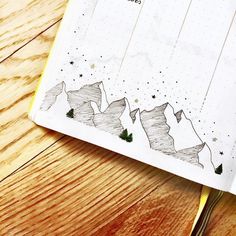 an open notebook with mountains and stars on the cover, sitting on a wooden table