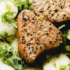 two pieces of meat with sesame seeds and cucumbers on a bed of lettuce