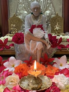 a statue sitting on top of a table covered in flowers and petals next to a lit candle