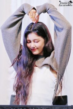 a woman with long hair standing in front of a keyboard and holding her hands behind her head