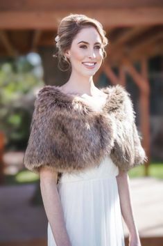 a woman in a white dress is wearing a fur shawl and smiling at the camera