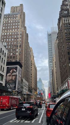 cars driving down a busy city street with tall buildings on either side and billboards in the background