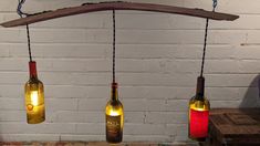 three wine bottles are hanging from a wooden beam with lights attached to the bottle holders