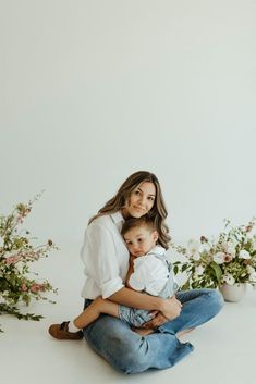 a woman sitting on the ground holding a baby in her arms and flowers behind her