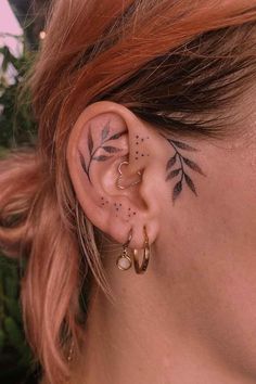 a woman with tattoos on her ear and behind the ear is a small leaf tattoo