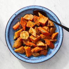 a blue bowl filled with cooked vegetables on top of a white countertop next to a black spoon