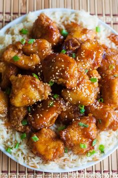 a white plate topped with rice covered in chicken and sesame seed sauce on top of a bamboo mat