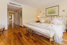 a large white bed sitting on top of a wooden floor next to a wall mounted painting