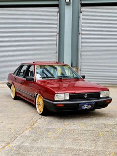 a red car parked in front of a building with yellow rims on it's tires