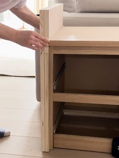 a person standing next to a wooden table with drawers on it and a couch in the background