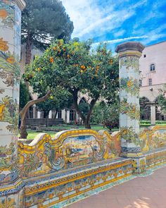 an orange tree is growing in the middle of a wall with colorful tiles on it