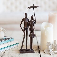 a statue of two people holding an umbrella next to a candle and some books on a table