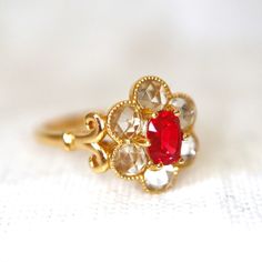 a gold ring with a red stone surrounded by white and clear stones on a white surface